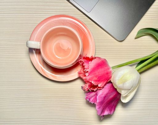 A flat lay of an aesthetic pink emptycoffee cup next to tulips and a laptop