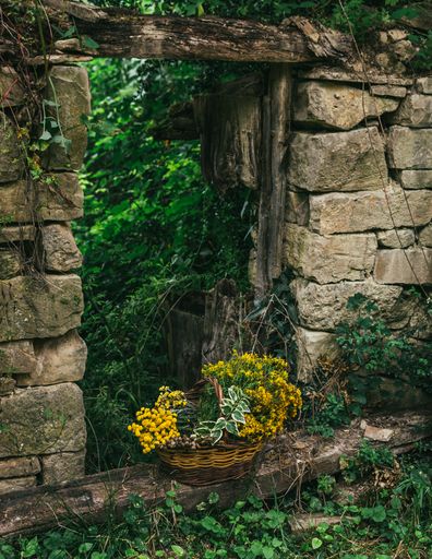 A vertical shot of a basket of flowers by a beautiful old stone wall with a wooden entrance
