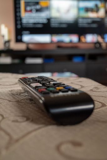 A closeup shot of a black remote control on the table with big screen T.V in the blurred background