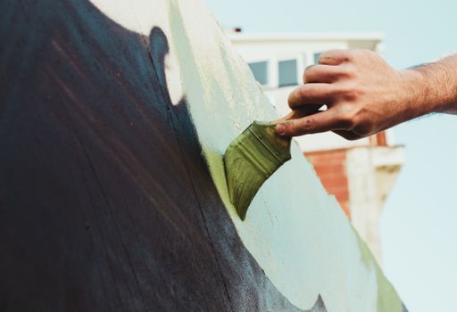 A low angle shot of a person painting a wall with white and black paint and a brush
