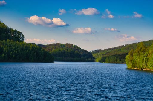 A natural view of a calm coast and green islands under a clear sunny sky