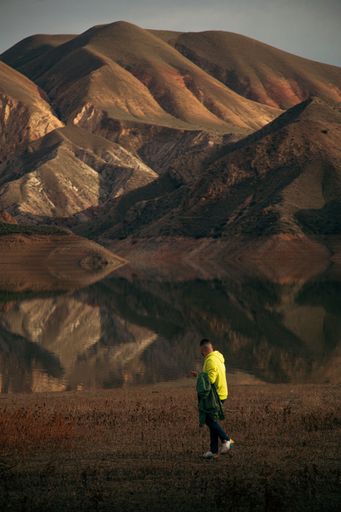 A vertical back view of young male looking at the mountain reflecting on a lake