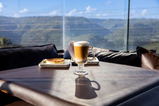 Table with a cappuccino and quiche breakfast in a coffee shop. Sunlight coming through glass window. Beautiful view of mountains in a sunny day