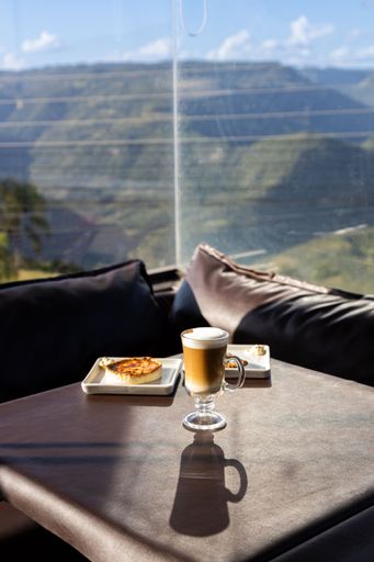 Table with a cappuccino and quiche breakfast in a coffee shop. Sunlight coming through glass window. Beautiful view of mountains in a sunny day