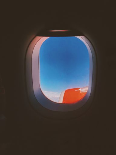 A vertical closeup shot of airplane wings shown through the window with beautiful clouds in the background