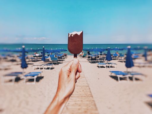A horizontal shallow focus closeup shot of a person holding a bitten chocolate ice-cream on the beach with a blurred background