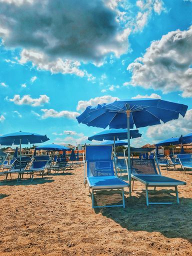 A vertical shot of blue parasols and sun loungers on the beach under the breathtaking cloudy sky