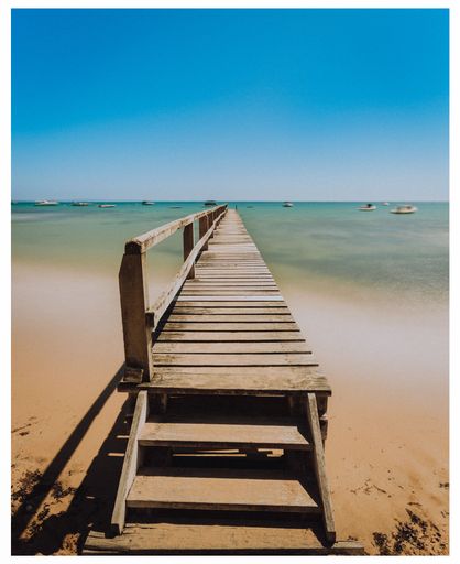 An old wooden pier stretching out from the white sands of the beach out to Port Phillip Bay