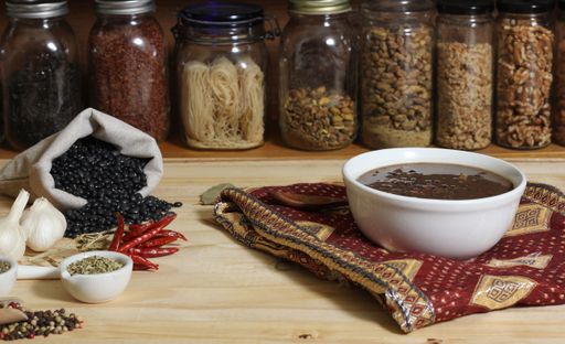 A bowl of black bean chili soup on a table with various herbs and spices