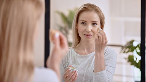 A Caucasian female applying tone cream in front of the mirror