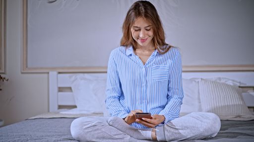 A young Caucasian female in pajamas using her smartphone while sitting in bed