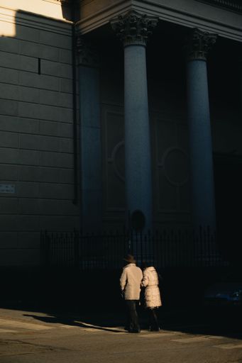 A back shot of a couple walking near a stone building on a sunny day