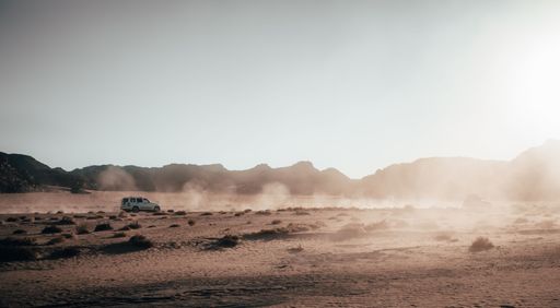 A white car driving in a desert during a beautiful sunrise