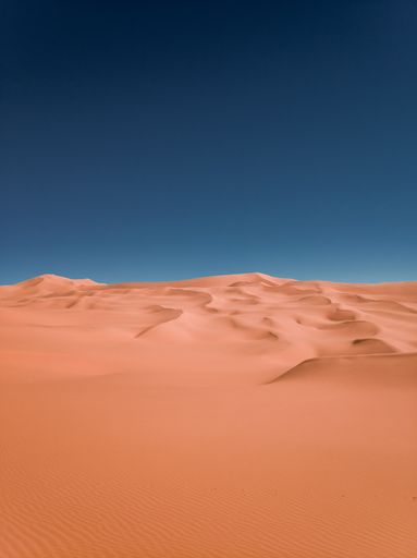A vertical shot of scenic sand dunes against a blue sky