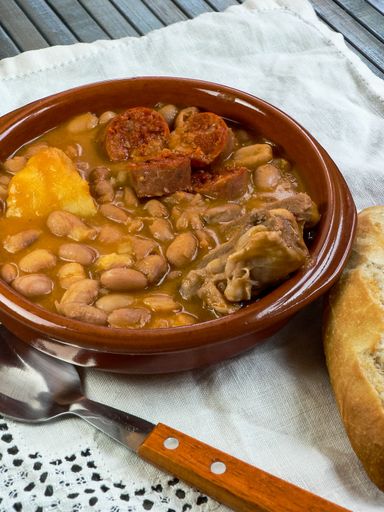A high angle shot of soup with beans and meat placed on the white blanket