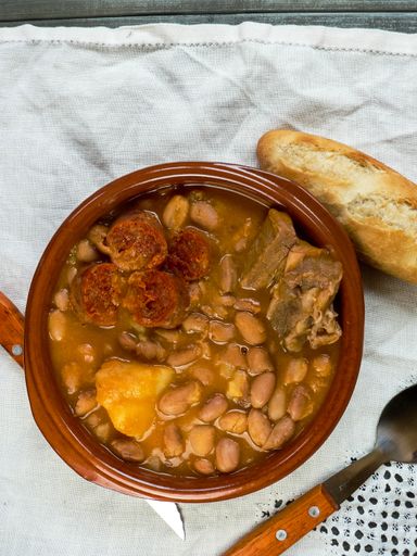 A high angle shot of soup with beans and meat placed on the white blanket