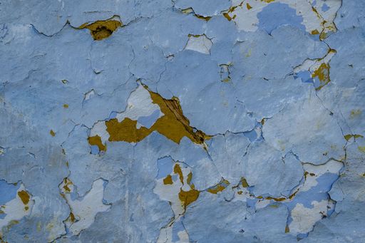 A close up shot of an old blue wall with cracks and paint chipping off