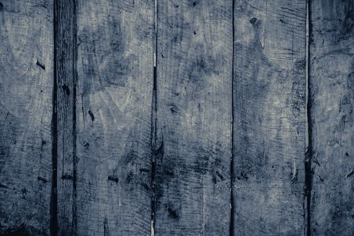 A closeup grayscale shot of wood panels of an old wooden fence with rusty nails in daylight