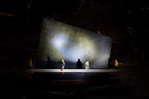 A closeup of small standing human figures on a black background with flashlight reflection