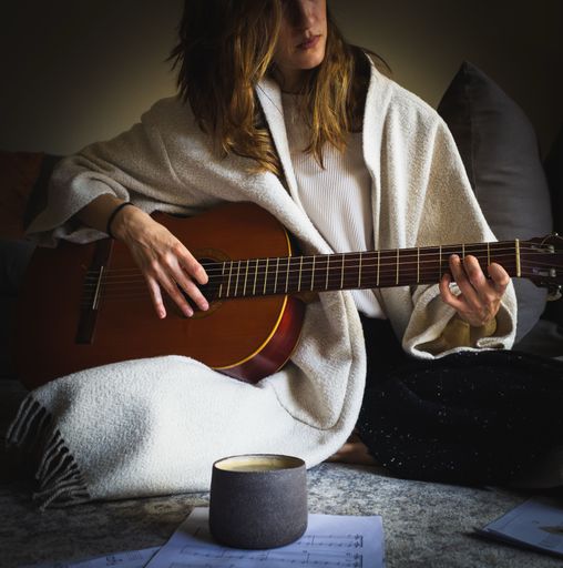 A girl playing the guitar while drinking her coffee in the early morning