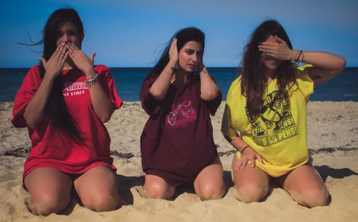 A horizontal shot of three young Hispanic women posing as three wise monkeys on a beach  - say no evil, hear no evil, see no evil