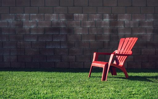 A horizontal shot of a red plastic chair on the grass in front of a bricked wall at daylight