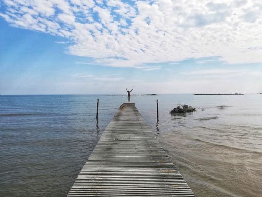 A horizontal shot of a happy person standing on the end of a wooden deck on a beach under puffy clouds
