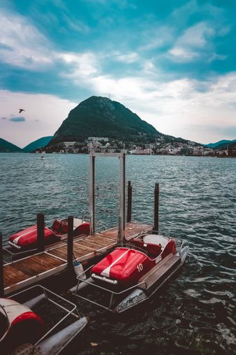 A vertical shot of pedal boats near a wooden dock on the sea surrounded by beautiful green mountains under the cloudy sky