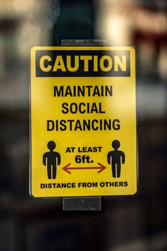 A vertical shot of a yellow sign warning to maintain social distance, at least 6ft