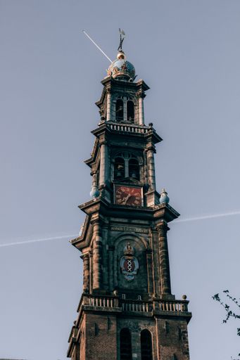 A vertical shot of a vintage bell tower against a blue sky in Amsterdam, Netherlands