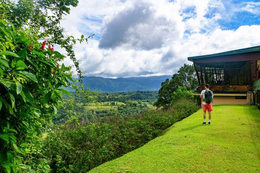 A man standing on a hill next to a house admiring the beautiful nature