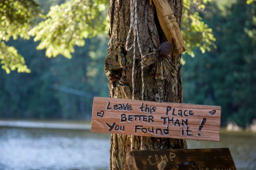 A closeup shot of a "leave this place better than you found it" sign hanging on a tree