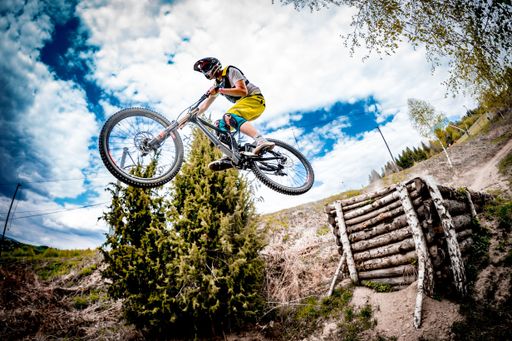 A male rider in a helmet on a bike doing an extreme jump over a track at a bike park in Kosutka