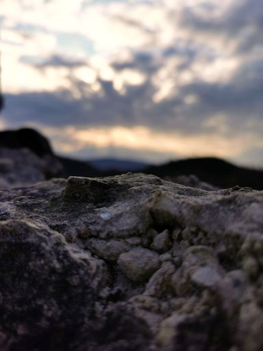 A vertical selective focus shot of a stone against cloudy sky at sunset