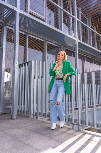 A vertical shot of a blonde model woman in a green jacket in a beautiful building in the city