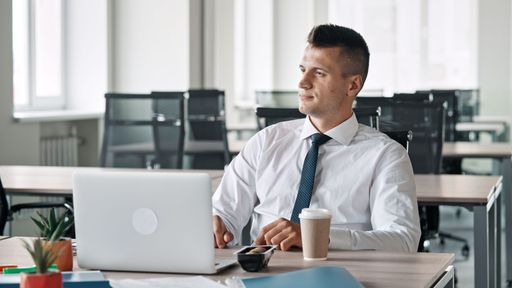 A man in a shirt and tie is sitting in the office in front of a laptop