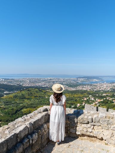 A vertical shot of Caucasian Woman looking at amazing view of city of Split in Croatia from Klis fortress.