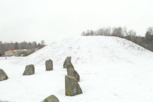 A view of gray rocks arranged in a circle in the middle of a rural area covered with snow and trees