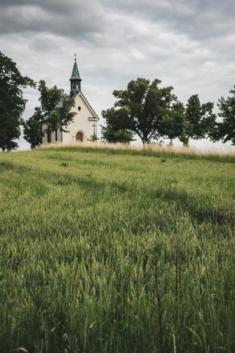 View to little chapel at top of green hill surrounded by trees under cloudy sky at Brno, Czech republic. Small Town Savior