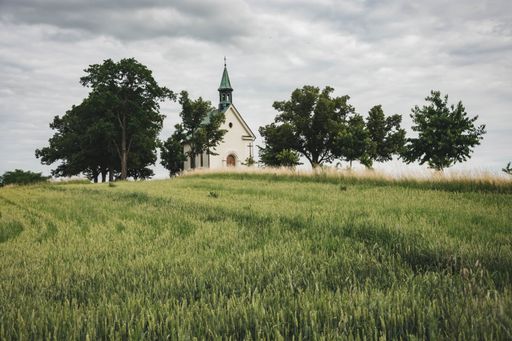 View to little chapel at top of green hill surrounded by trees under cloudy sky at Brno, Czech republic. Small Town Savior