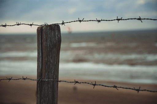A long fence with wooden poles and barbed wire on the beach on blurry background of the sea