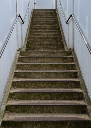 Looking up at a concrete stairway with handrails. An urban, outdoor set of steps with metal handrails.