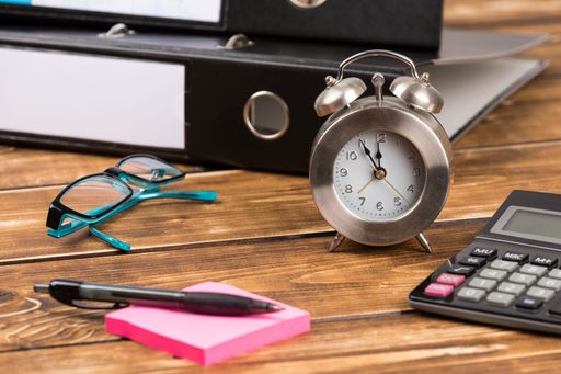 A table with office supplies, glasses, and a clock - time is money concept