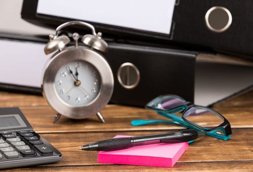 A table with office supplies, glasses and a clock - time is money concept