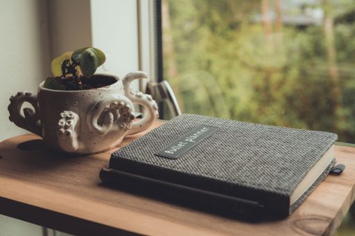 A beautiful shot of a bullet planner and a ceramic pot neat the window