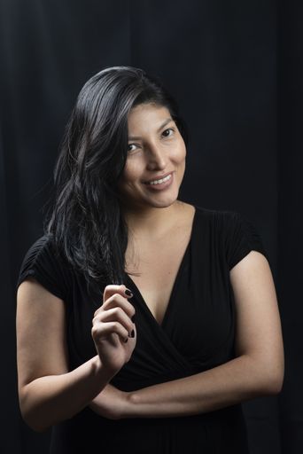 A portrait of a smiling Hispanic female in a black dress under the lights