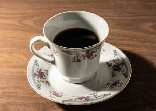 A closeup shot of an eastern coffee cup filled in half and a saucer on a brown table
