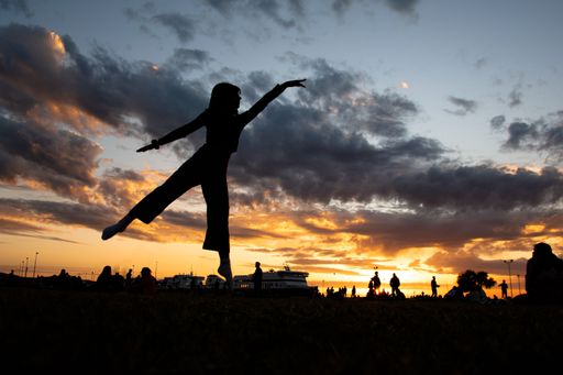 A silhouette of a girl dancing and jumping in the air on a sunset sky background in Patra, Greece