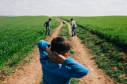 A view of three schoolboys playing street football in a green field in Hatay Province, Turkey
