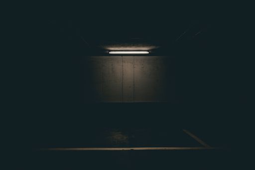 A horizontal shot of a lighted fluorescent tube in a parking lot on a ground level at night time